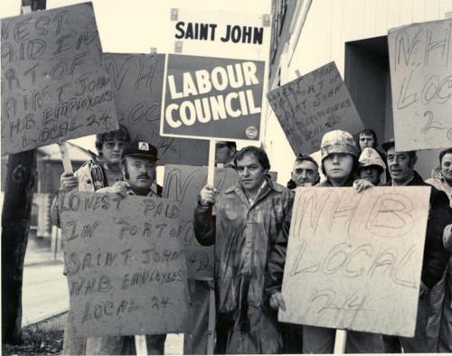 National Day of Protest -- October 14th, 1976 -- organized by the Canadian Labour Congress, to protest the federal government's wage control legislation. In the early hours the President of the Saint John District Labour Council, George Vair, gathers with the port workers on the lower west side in preparation for their march over the Saint John Harbour Bridge. On his right side is Wayne Hall and on his left is David Shannon, both members of the National Harbour Board (CLC), Local 24.